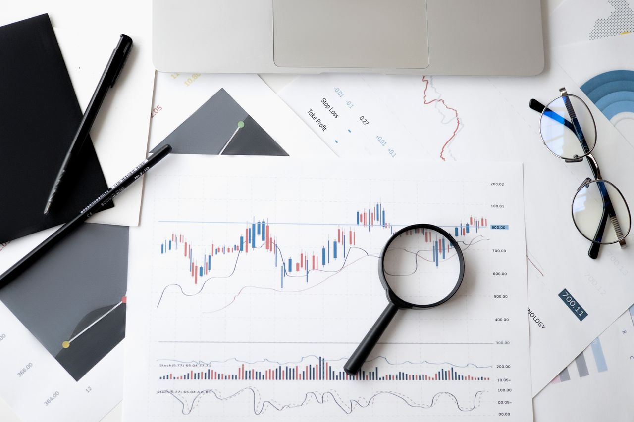 Vue à plat de documents d’analyse boursière avec loupe, stylos et lunettes.